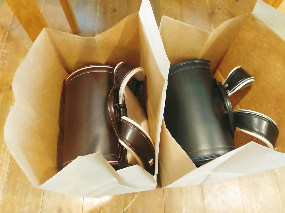 紙袋に入った茶色とピンクの女の子用のランドセルと黒色と青の男の子用のランドセル